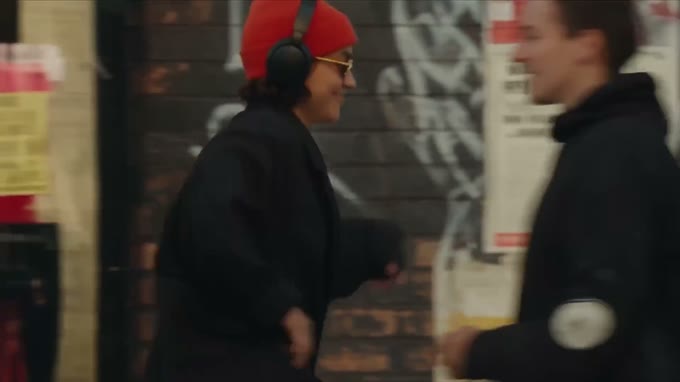 Close shot from the side: the same woman passes a brick wall, her face in profile.