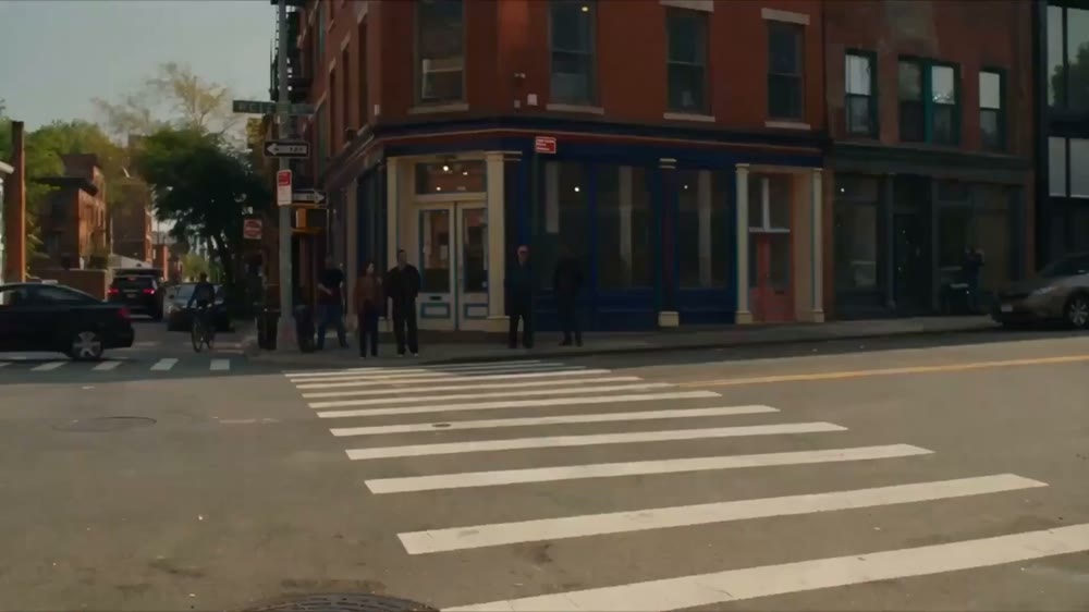 First frame of the street film: an empty crossing on a sunlit corner, a few people on the far pavement.